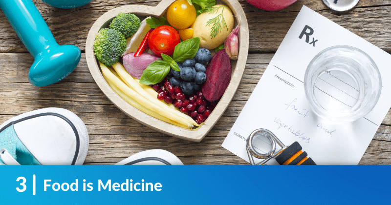 A heart-shaped bowl of fruits and veggies, alongside weights and other objects related to maintaining good health. Heading reads, “Food is Medicine"